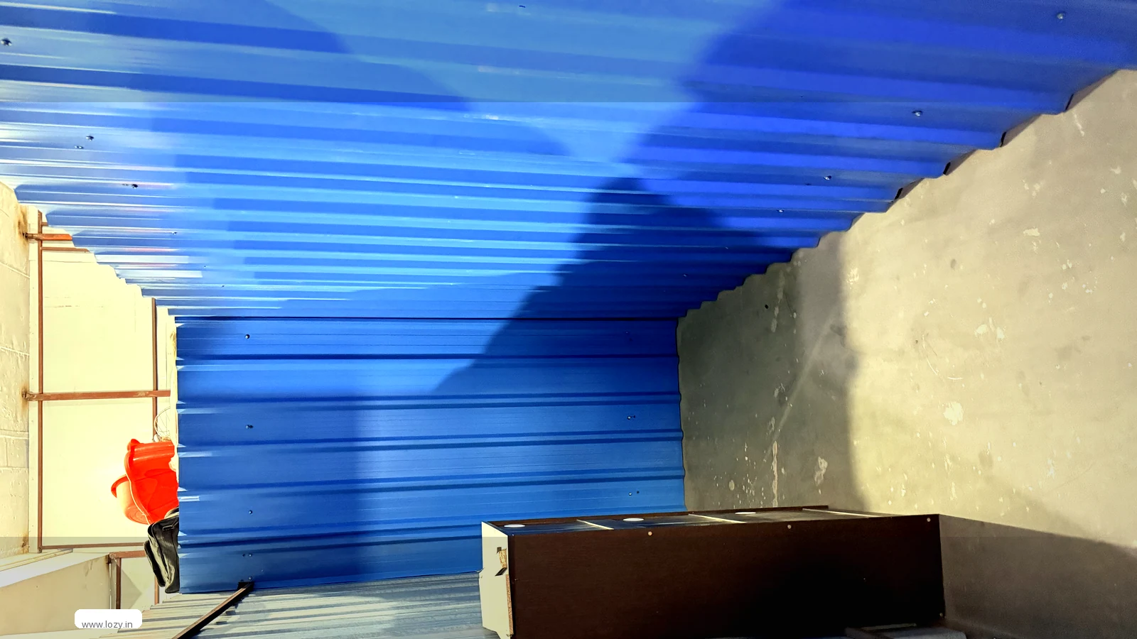 Lozy self-storage corridor at the Gurugram facility - individually numbered units behind solid roller doors on a blue painted floor, with a marked walkway and strip lighting overhead