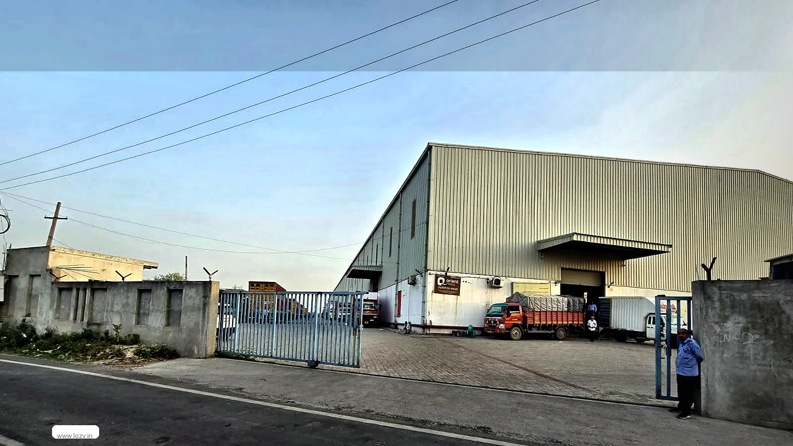 Gated frontage of a Lozy warehouse near Murthal in Sonipat, Haryana - concrete compound wall, part-open sliding gate and a cream ribbed-clad shed behind
