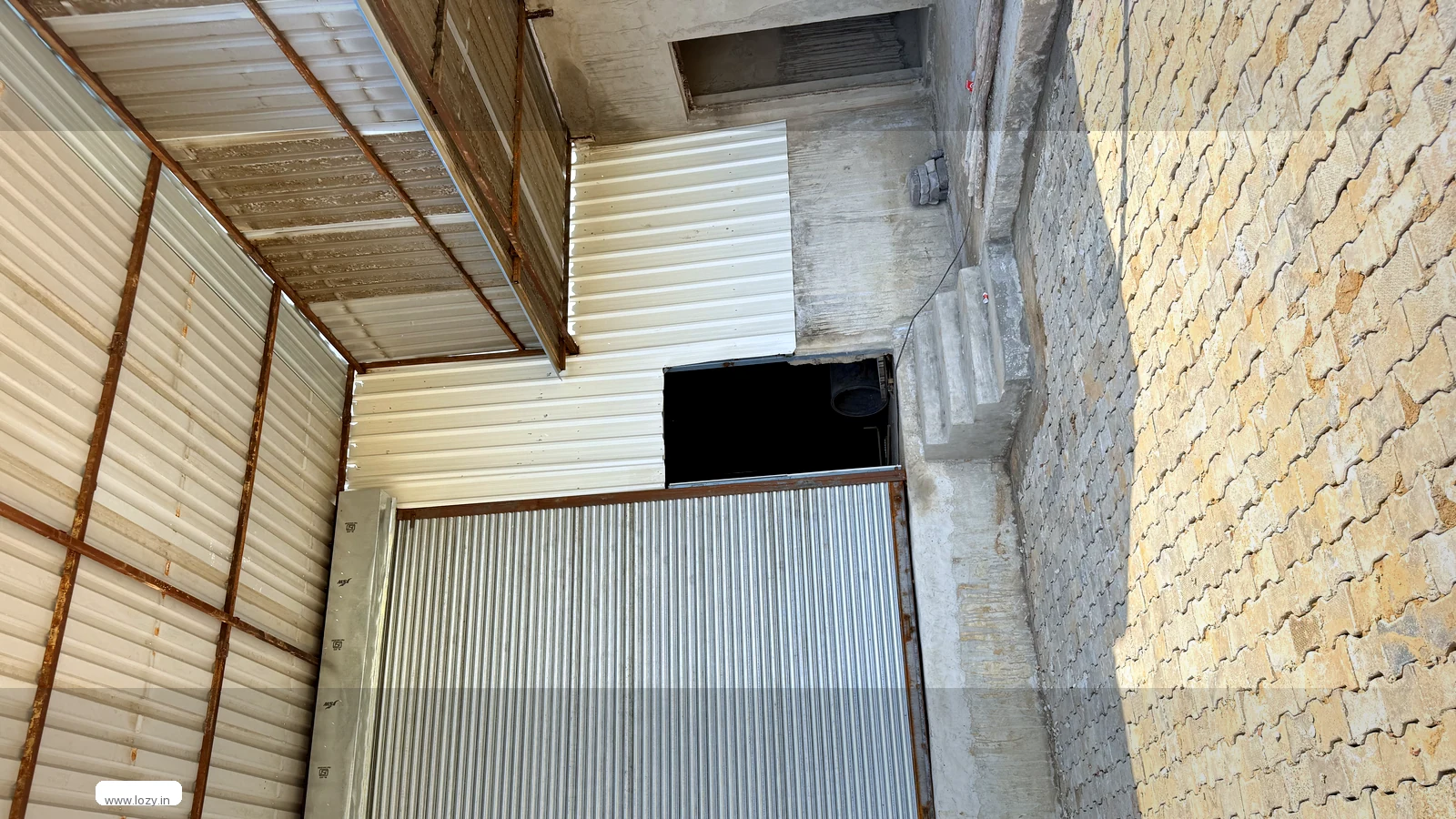 Lozy warehouse at Kherki Daula, Gurugram - a closed roll-up shutter in a steel frame, corrugated metal wall cladding on a concrete plinth and a paver apron
