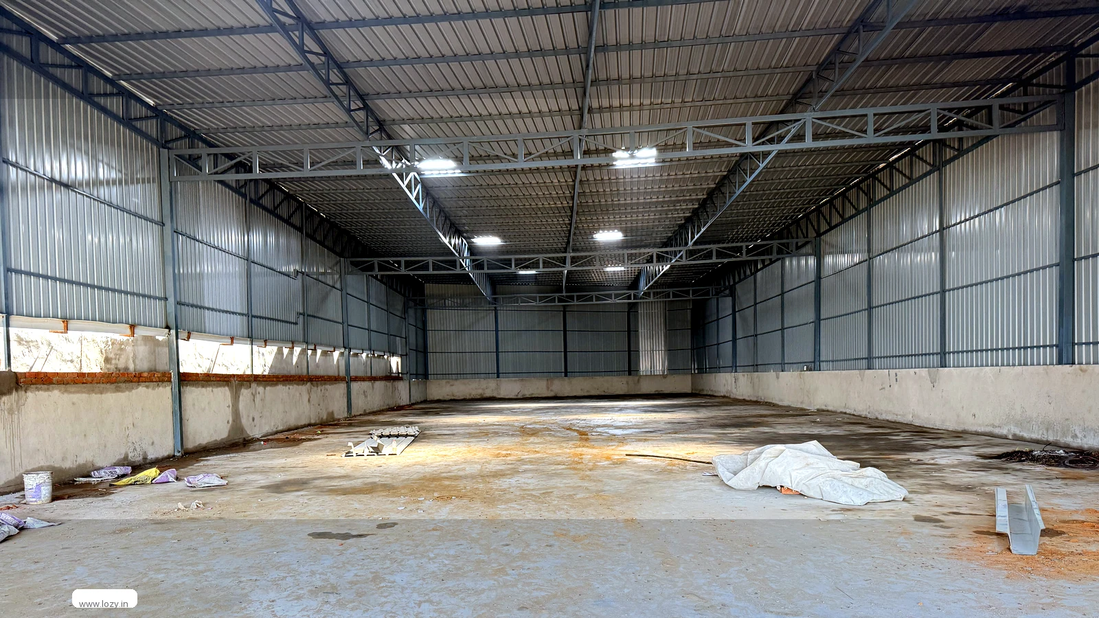 Empty clear-span warehouse unit at Manesar M Zone, Gurugram - steel trusses, bare concrete slab and strip lighting