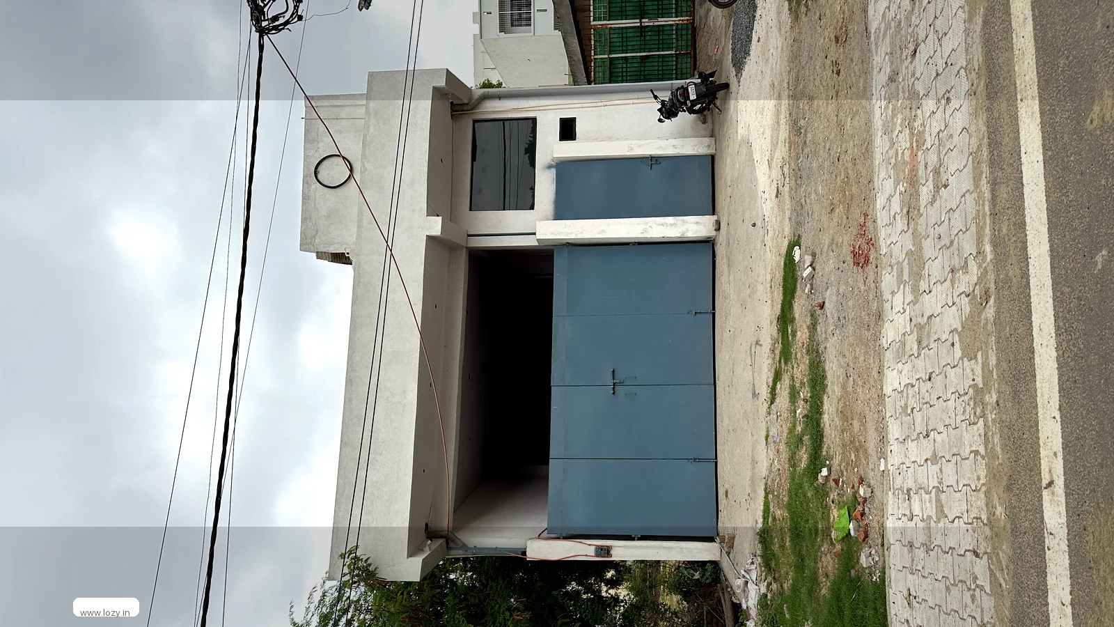 Storage unit with a wide blue-grey roller shutter and a paver apron in front, the ground a loaded vehicle stands on