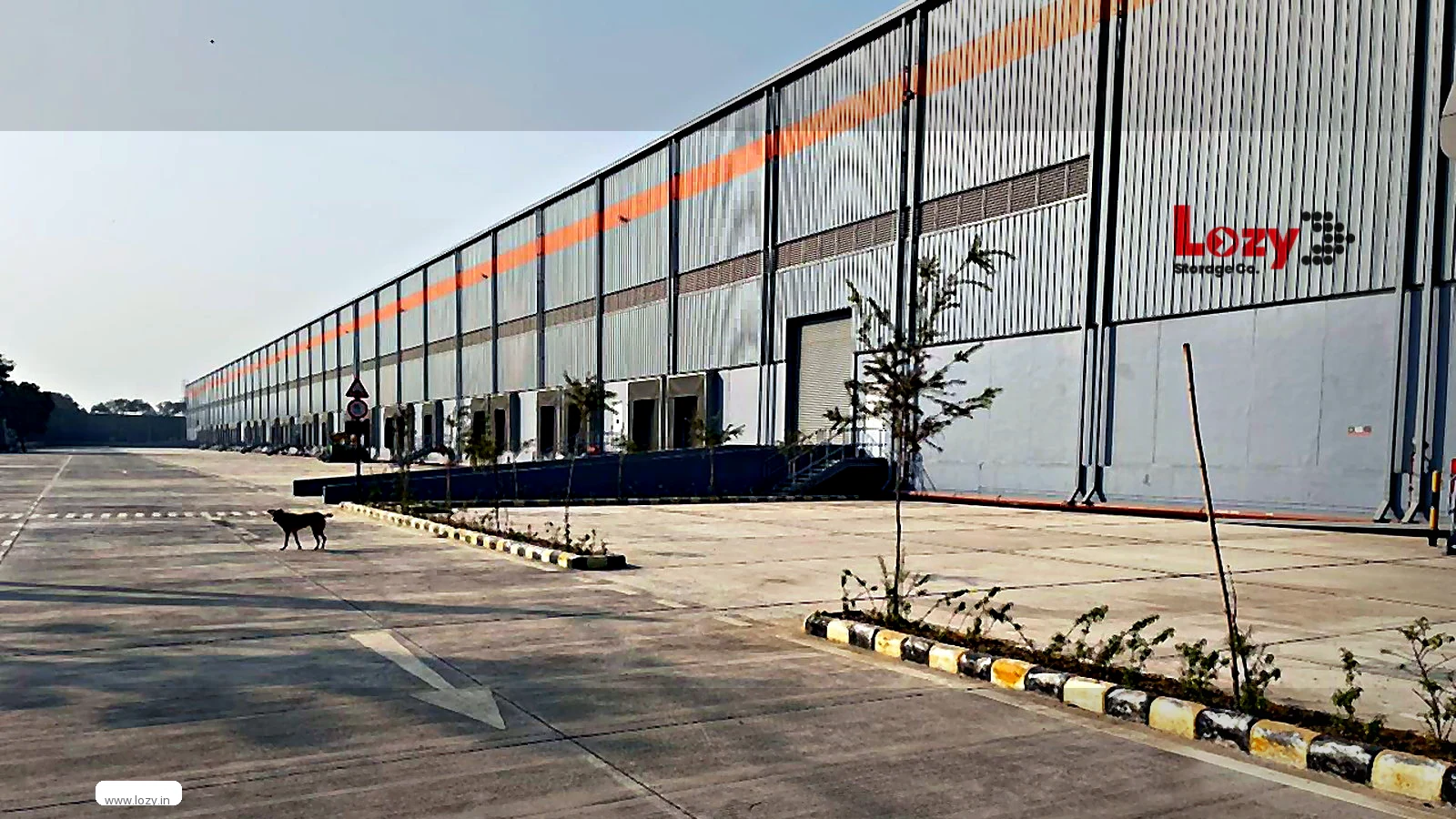 Row of closed roller-shutter loading docks along a grey-clad warehouse at Alipur, north Delhi, with an empty concrete apron and a Lozy sign