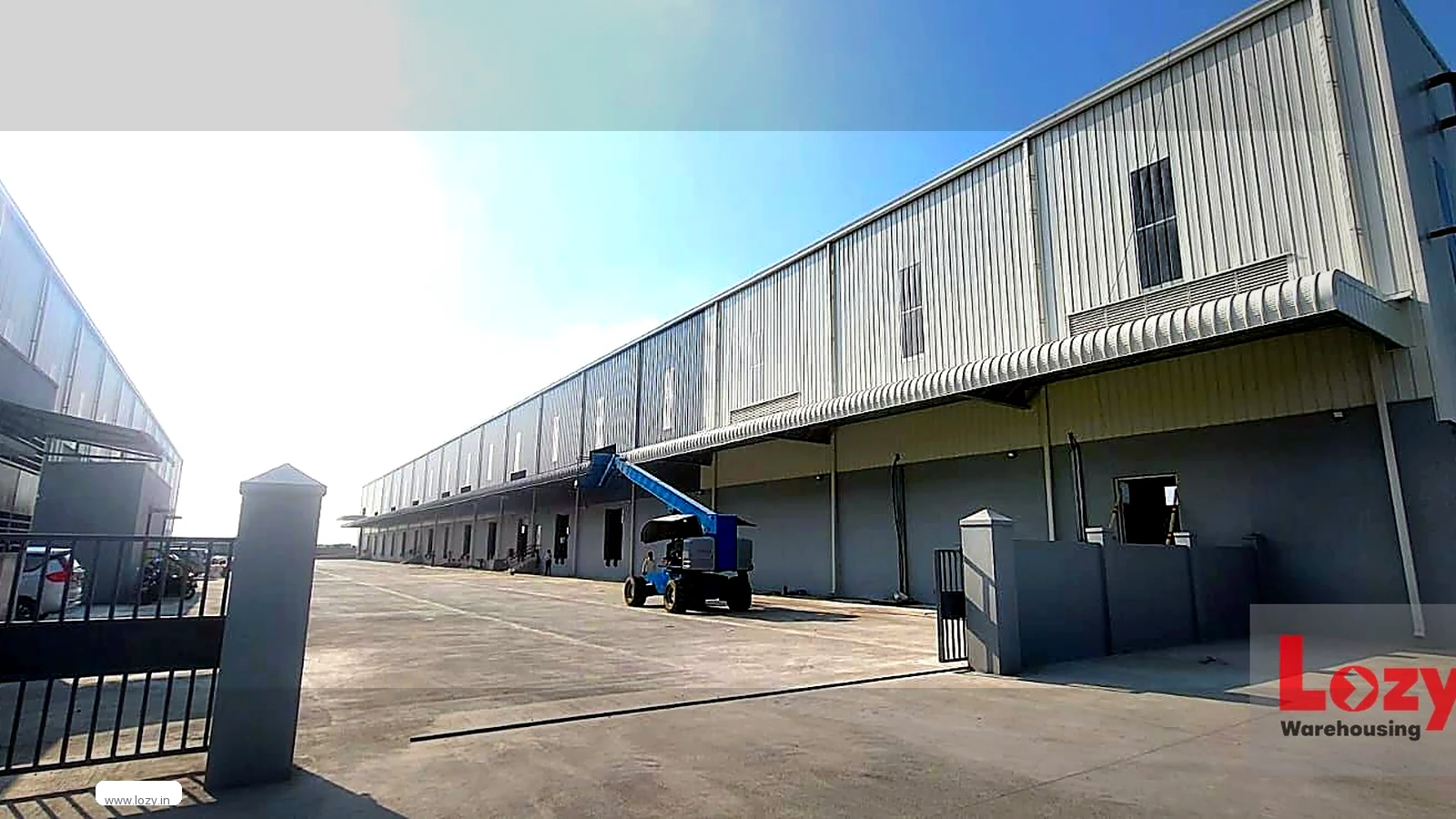 A Lozy warehouse block with a run of roller shutters on a ribbed metal-clad elevation and a wide concrete yard with gate pillars