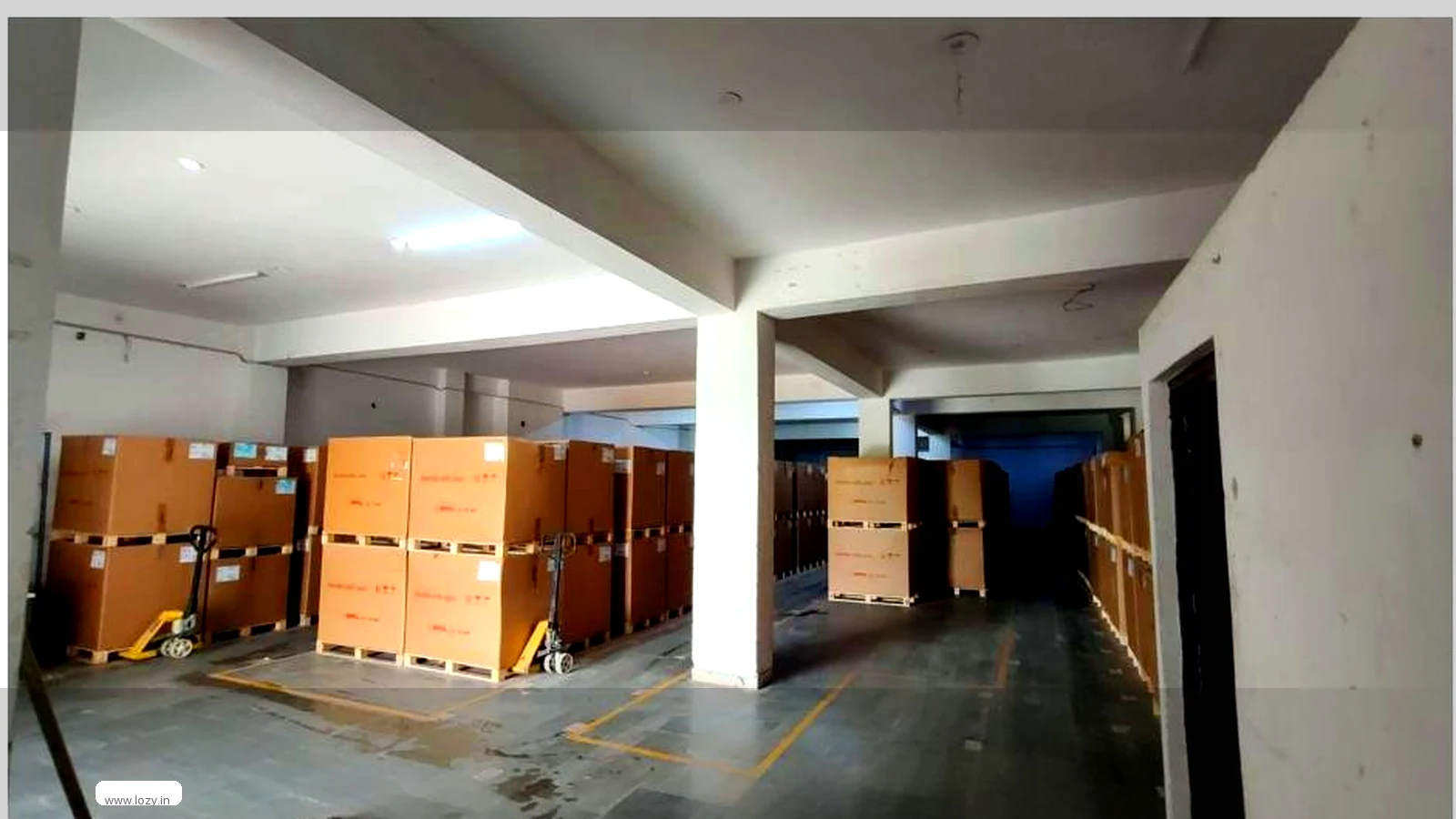 An ambient storage floor in Lozy's network: painted bay markings on a raised tiled deck, ceiling fans and shrink-wrapped cartons stacked clear of the aisles