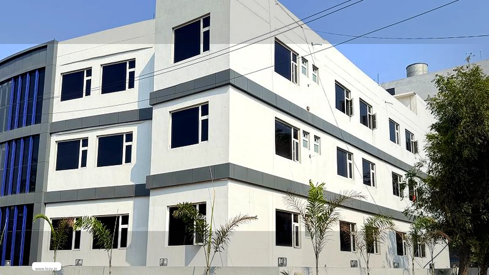 A white multi-storey commercial building behind a fenced compound with palm trees, one of the monitored buildings Lozy's managed storage floors sit in